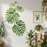 Indoor setting with various potted plants and a large green leaf wall decal.