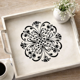 Decorative tray with a black floral design on a wooden surface with a cup of coffee and flowers.