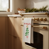 Decorative towel with Christmas tree design hanging on a kitchen oven handle.