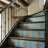 A rustic wooden staircase with light blue painted steps decorated with gold fleur-de-lis motifs, dark metal balusters, and a blue-and-white gingham runner at the bottom.