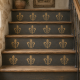 A set of dark charcoal gray painted stairs decorated with repeating gold fleur-de-lis motifs, featuring natural wood treads and a black metal railing.