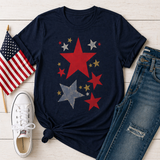 Navy blue t-shirt with star design, American flag, white sneakers, and jeans on a wooden surface