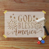 Stencil with 'God Bless America' text on a wooden surface, craft paints and a paint roller