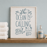 Framed artwork with 'The Ocean is Calling and I Must Go' quote on a shelf with towels and a bottle.