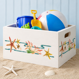 Toy storage box with beach-themed design filled with toys on a sandy surface.