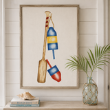 Framed artwork of a paddle and buoys on a wall with a window view of the ocean.