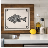 Decorative fish wall art on a kitchen counter with a lemon and bottles.