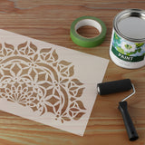 Mandala stencil with intricate floral pattern on a wooden surface with painting supplies surrounding it.