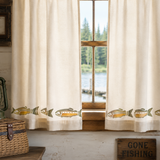 Curtains with fish designs in front of a window with a view of water and trees.