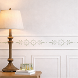 Decorative wall stencil design on a white wall with a lamp and wooden side table.