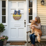 Woman sitting on a bench with a dog in front of a white door with a decorative wreath.