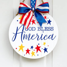 God Bless America Round Sign Stencil painted onto a white wooden sign with patriotic ribbon