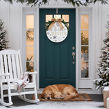 Dog lying on a rug in front of a decorated door with 'Hello Winter' sign, surrounded by Christmas trees and a rocking chair.