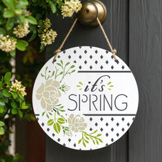 Decorative stencil of a round spring sign hanging on a door, featuring floral designs and welcoming text.