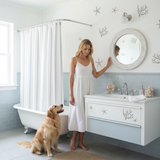 Woman in a white dress standing in a bathroom with a dog, looking at herself in a round mirror.