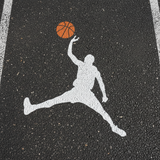 White silhouette of a basketball player in mid-air with a basketball on black asphalt.