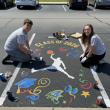 Two people painting a colorful design on pavement with 'Class of 2026' text.