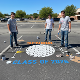 Three students in gray t-shirts and jeans standing on a school parking lot with 'Senior Class of 2026' painted on the ground.