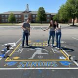 Three students in a parking lot with a 'Class of 2026 Seniors' mural.
