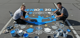Two people painting a 'Senior 2021' design on a pavement.