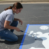 high school student applying the volleyball player stencil to a  high school parking spot