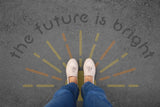 Person standing on pavement that has been stenciled with 'The Future is Bright' text.