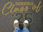 Person standing on pavement that has been stenciled with 'Seniors Class of '26' text.