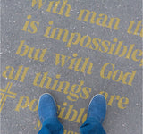 Person standing on pavement that has been stenciled with the Matthew Bible Verse text.