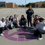 Purple peace symbol on a pavement background with high school students around the design