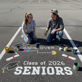 Two people painting 'Class of 2026 Seniors' on a pavement with graduation symbols.