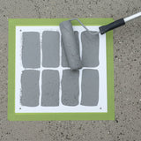 Roller and gray paint swatches on a white sheet with green border against a concrete background