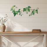 Wall stenciled pattern of ivy on a white wall above a wooden bench with a vase and books.