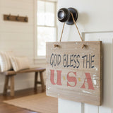 God Bless the USA Stencil stenciled onto a door sign hanging on a door knob.