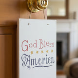God Bless America Wall Stencil stenciled onto a square wooden sign hanging on a door knob.